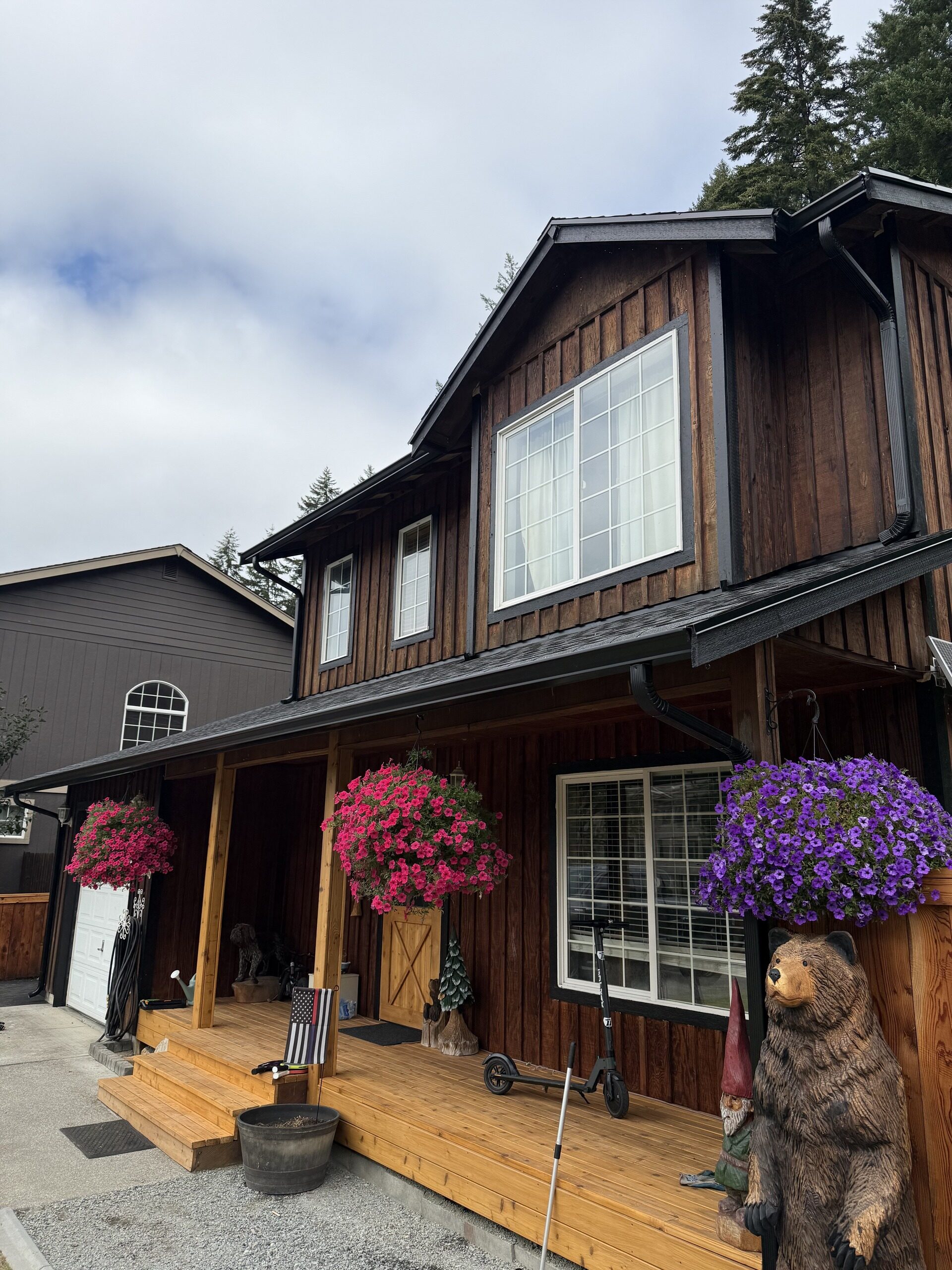 Cedar-sided lodge-style home with dark seamless gutters and downspout under an overcast Pacific Northwest sky
