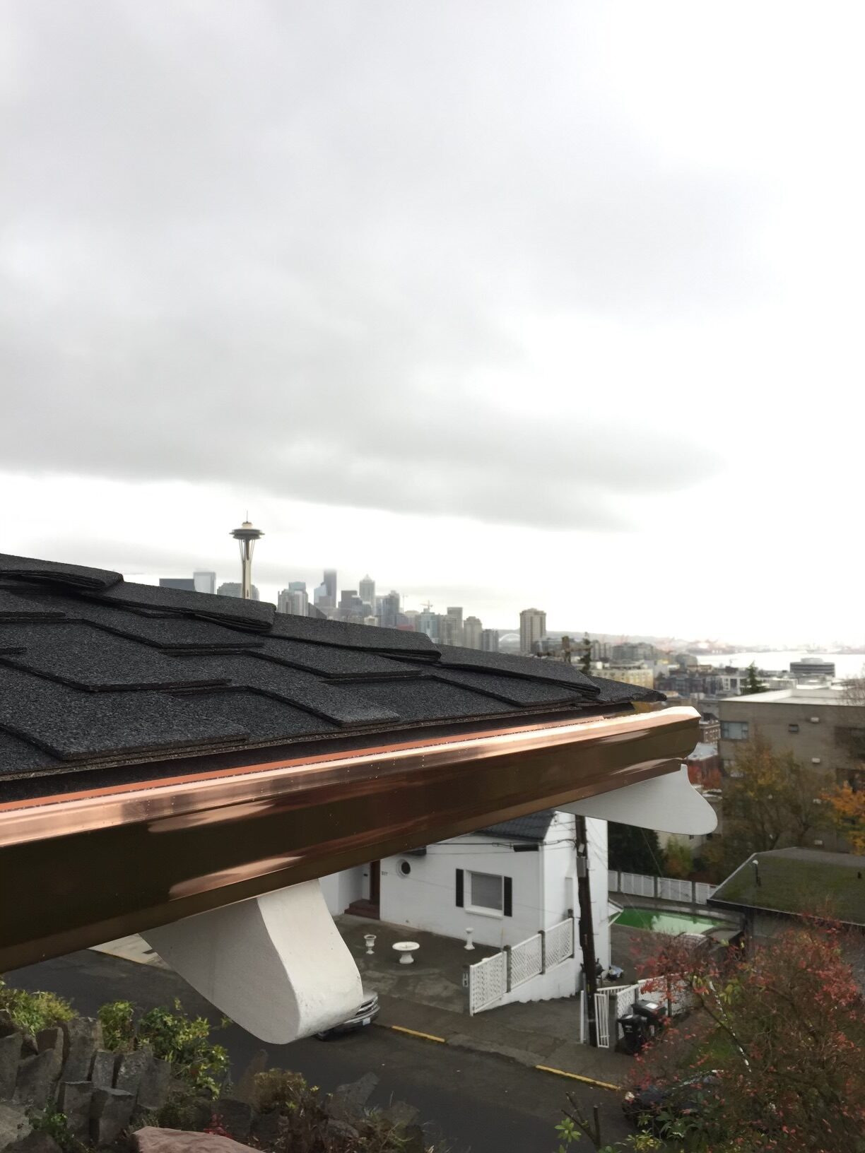 Copper gutter installation detail with Seattle skyline and overcast Pacific Northwest sky