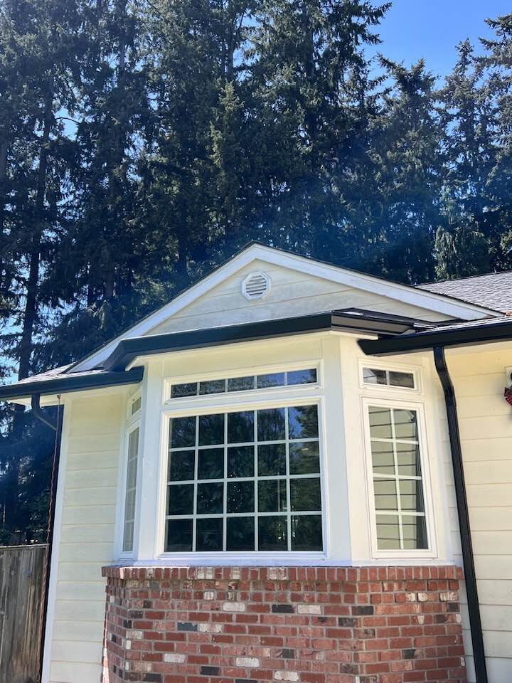 Gable end of residential home with dark seamless gutters and PNW conifers