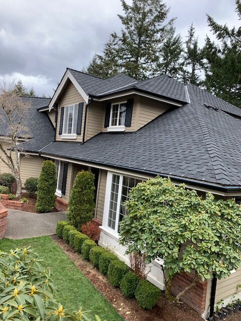 Home with dark roof and seamless gutter system surrounded by mature landscaping