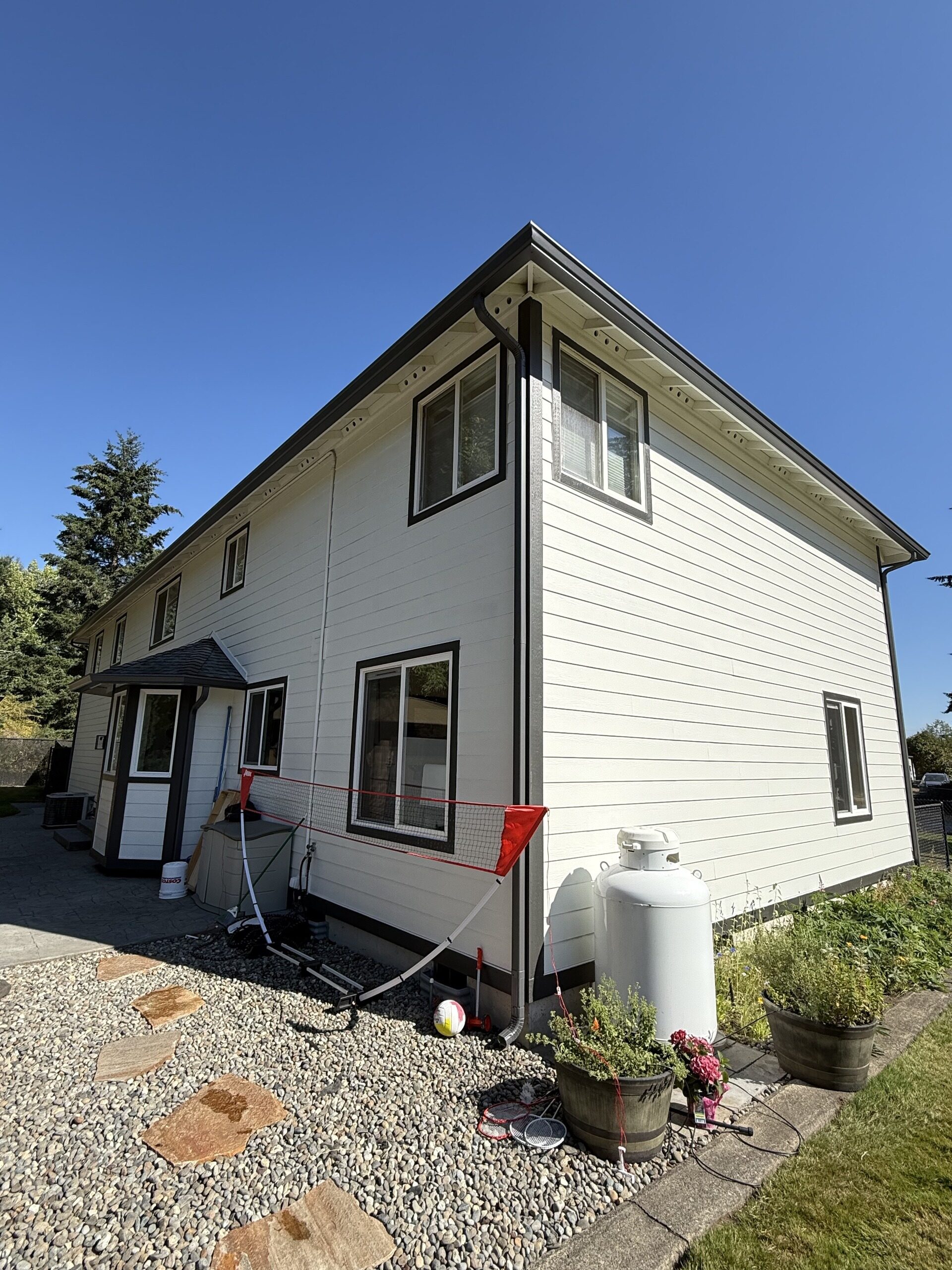 White farmhouse with dark trim, new gutters along the eave, and a downspout carried to grade