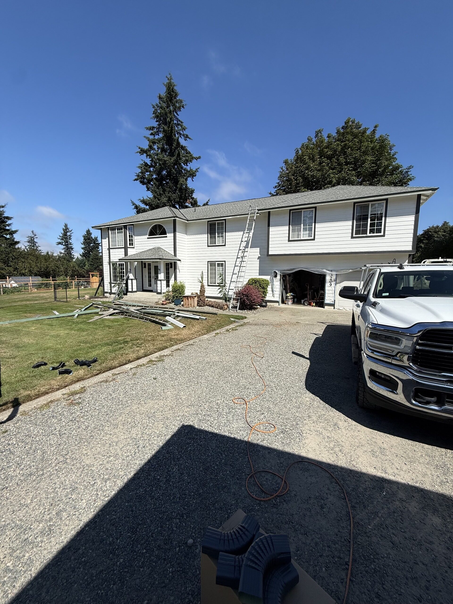 Before: two-story home with its old gutters stripped off and stacked on the lawn beside the work truck and ladder