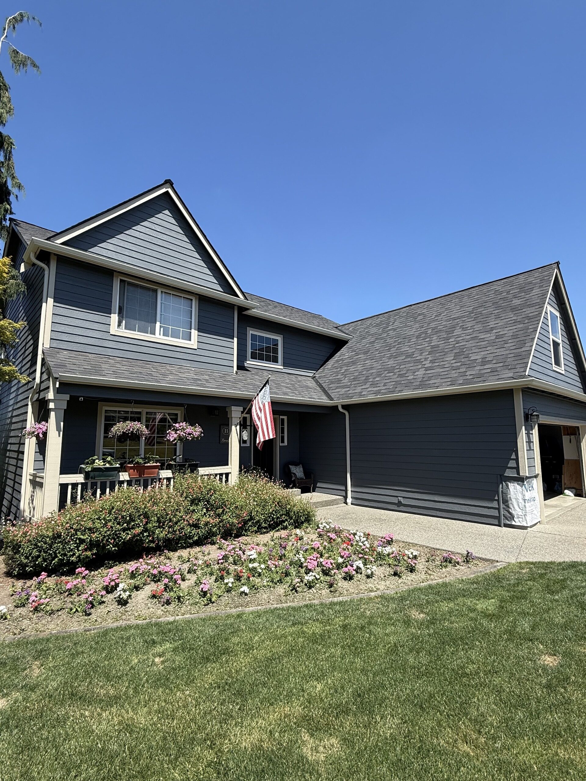 Navy two-story home with dark seamless gutters above a covered porch and flower beds